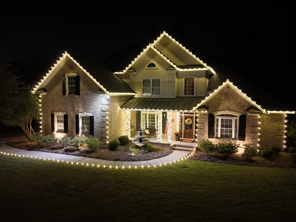 Two-story brick home with full roofline lighting, arched entry, and pathway lights leading to the door